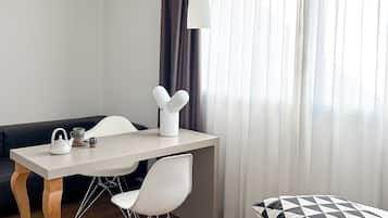 A modern hotel room with a bed, a desk with chairs, a sofa, and a large window with curtains.
