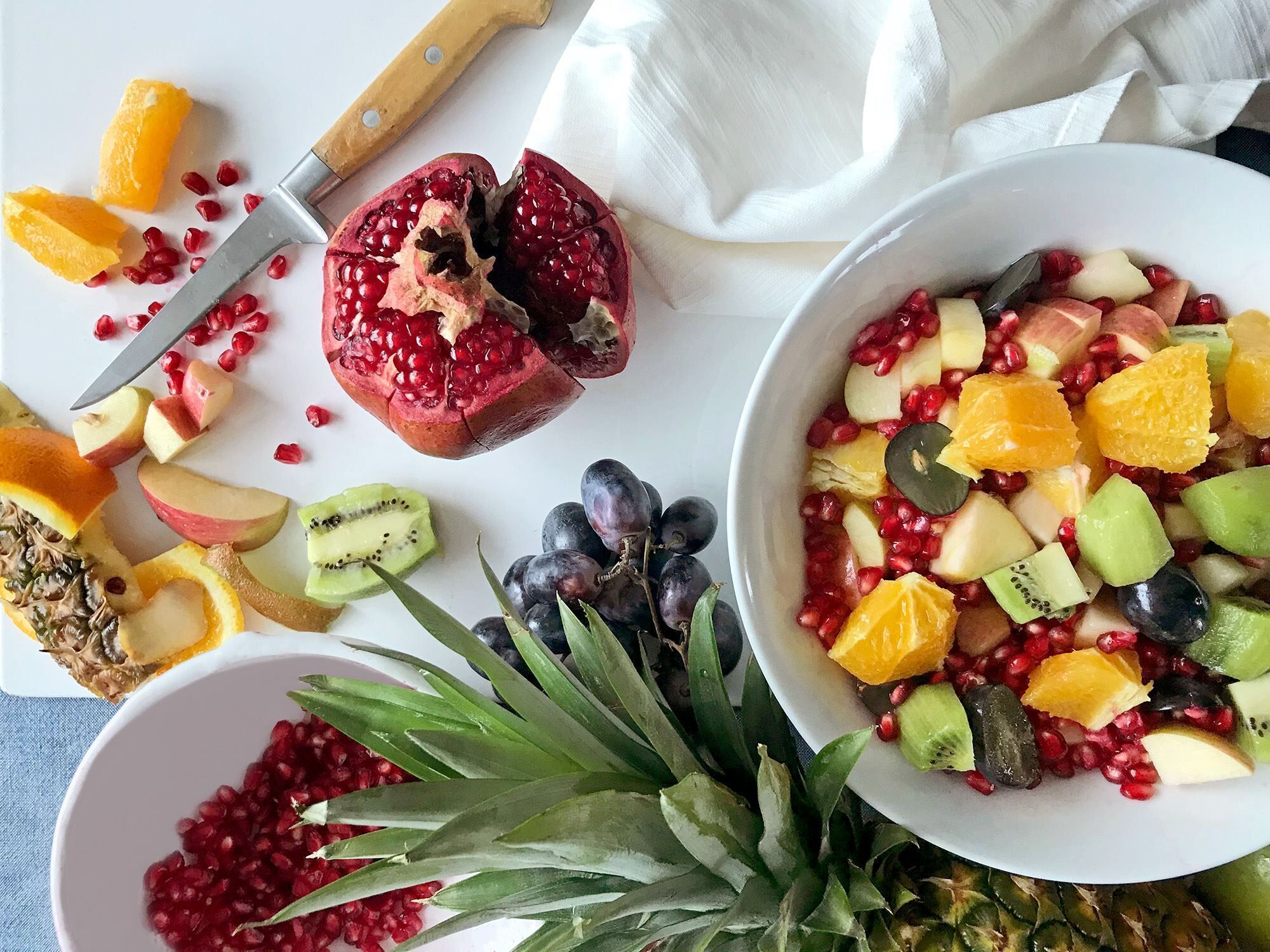 A bowl of mixed fruit salad with pomegranate seeds, kiwi, grapes, and orange segments.