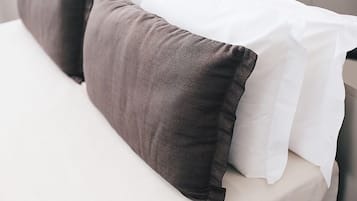 Una cama con un colchón blanco y dos almohadas, una oscura y otra clara.