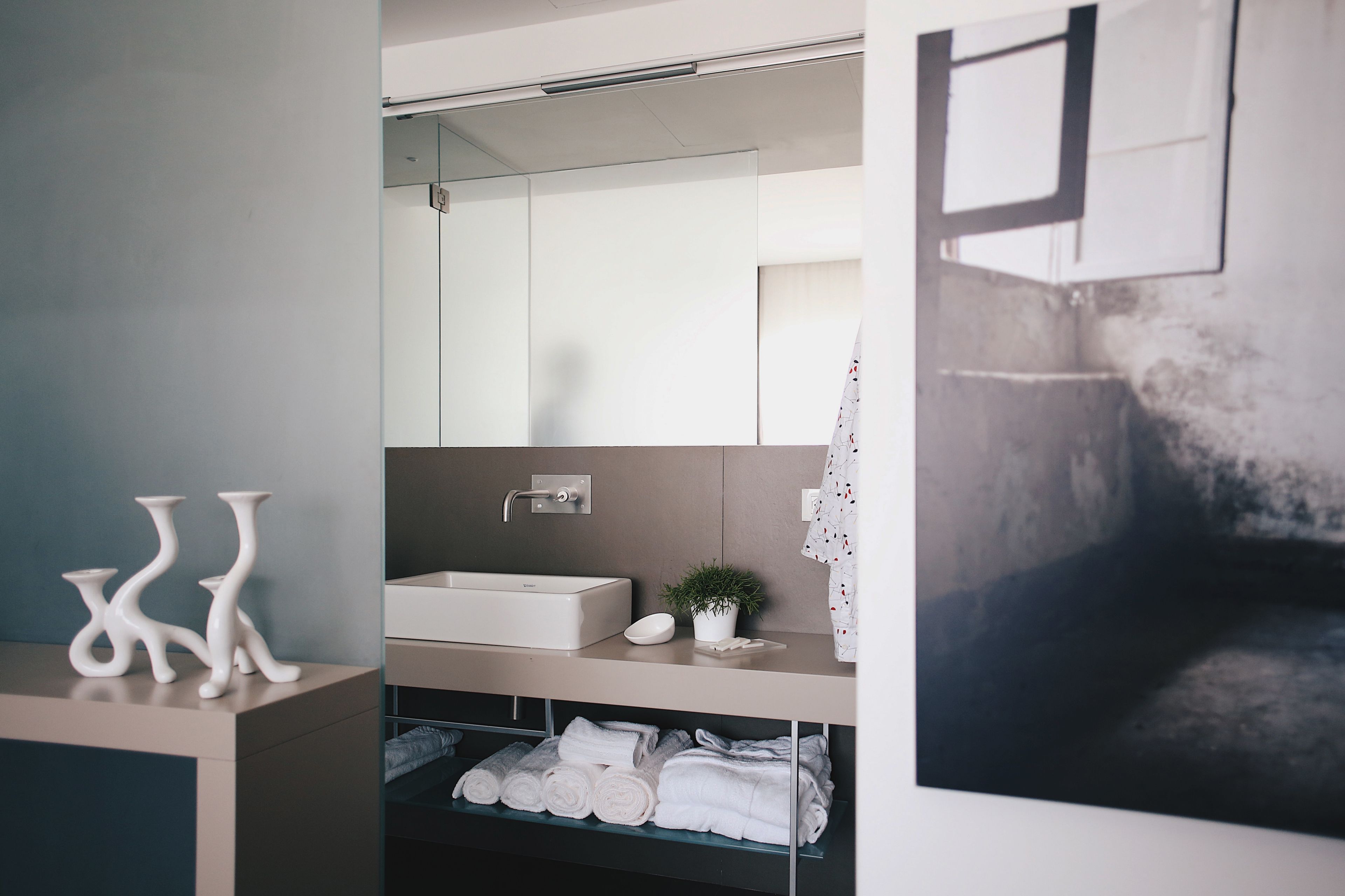 Une salle de bain moderne avec un grand miroir, un lavabo blanc et des serviettes soigneusement pliées sur une étagère.