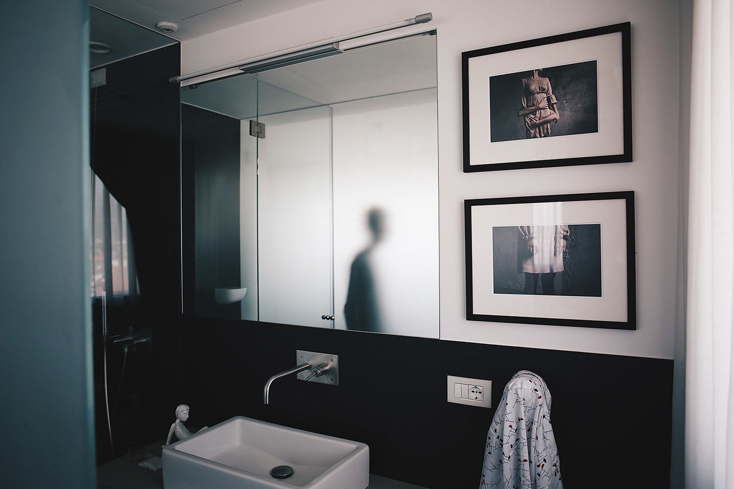 Un baño moderno con un espejo grande, un lavabo blanco y dos cuadros enmarcados en la pared.