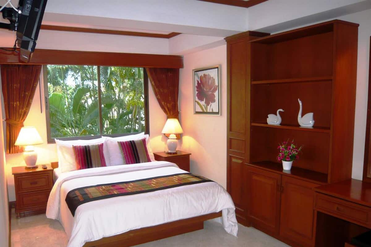 A bedroom with a bed, two bedside tables, a nightstand, a wooden cabinet, and a window with curtains.