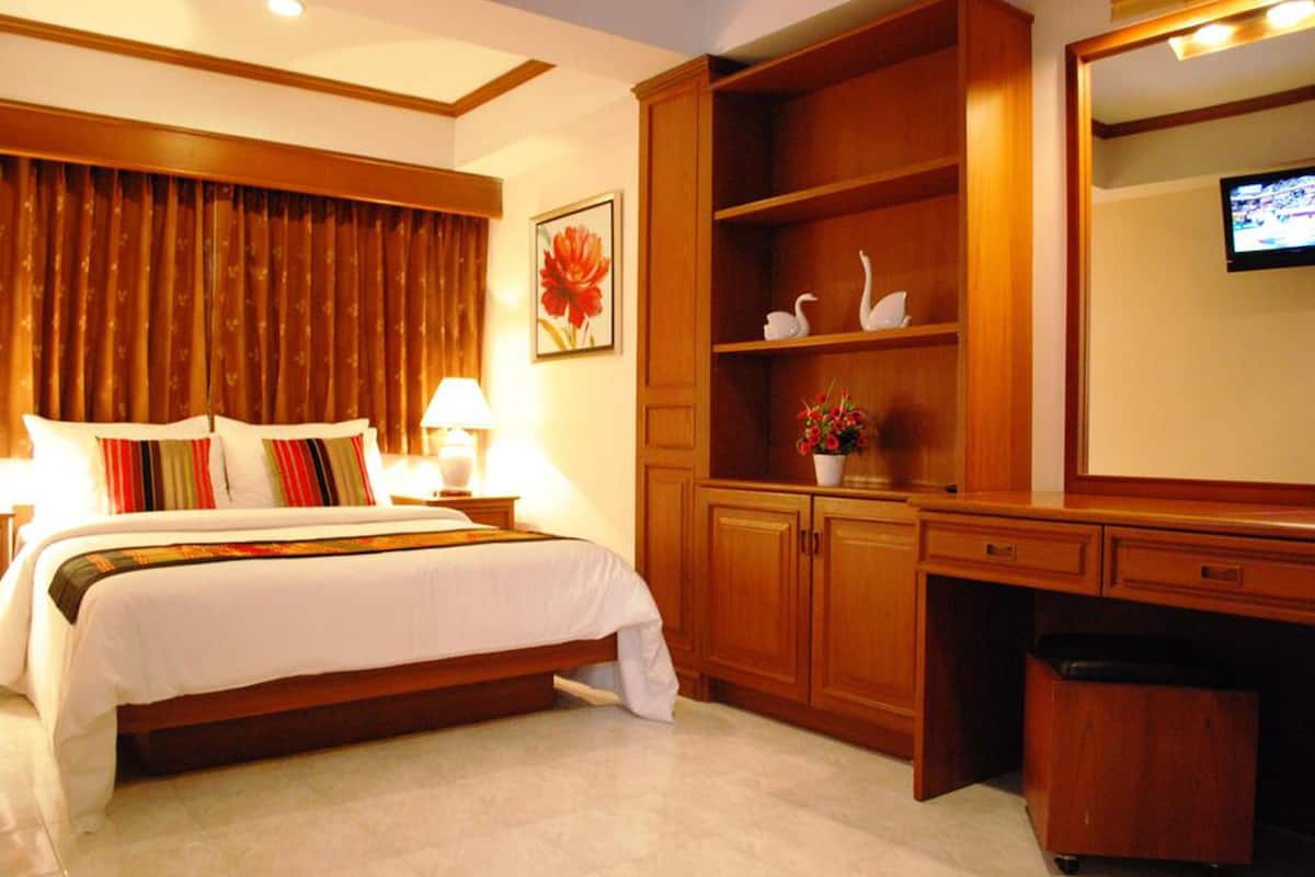 A hotel room with a bed, wooden wardrobe, a desk, a television, and a flower vase.