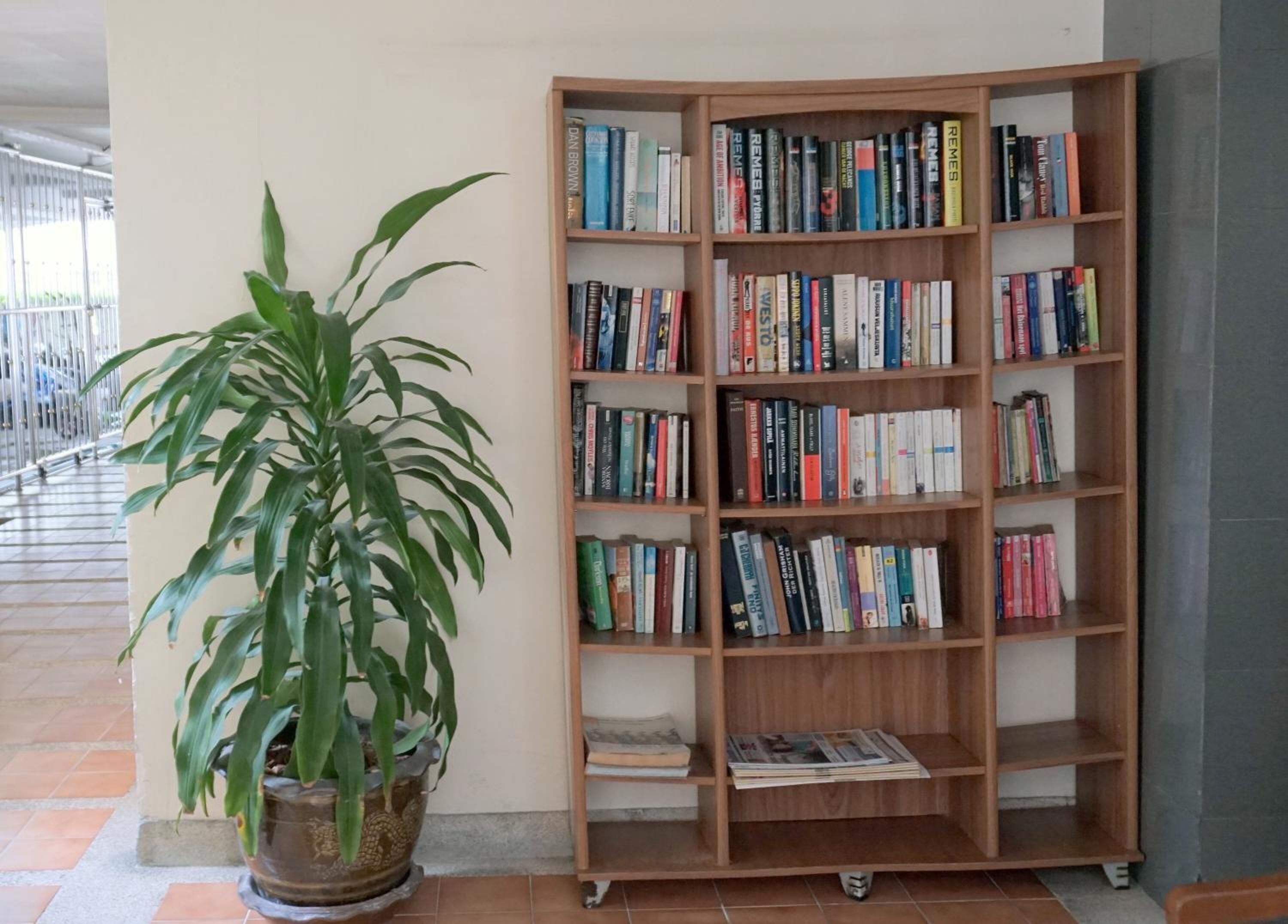 A corner bookshelf filled with books, a potted plant, and a tiled floor.