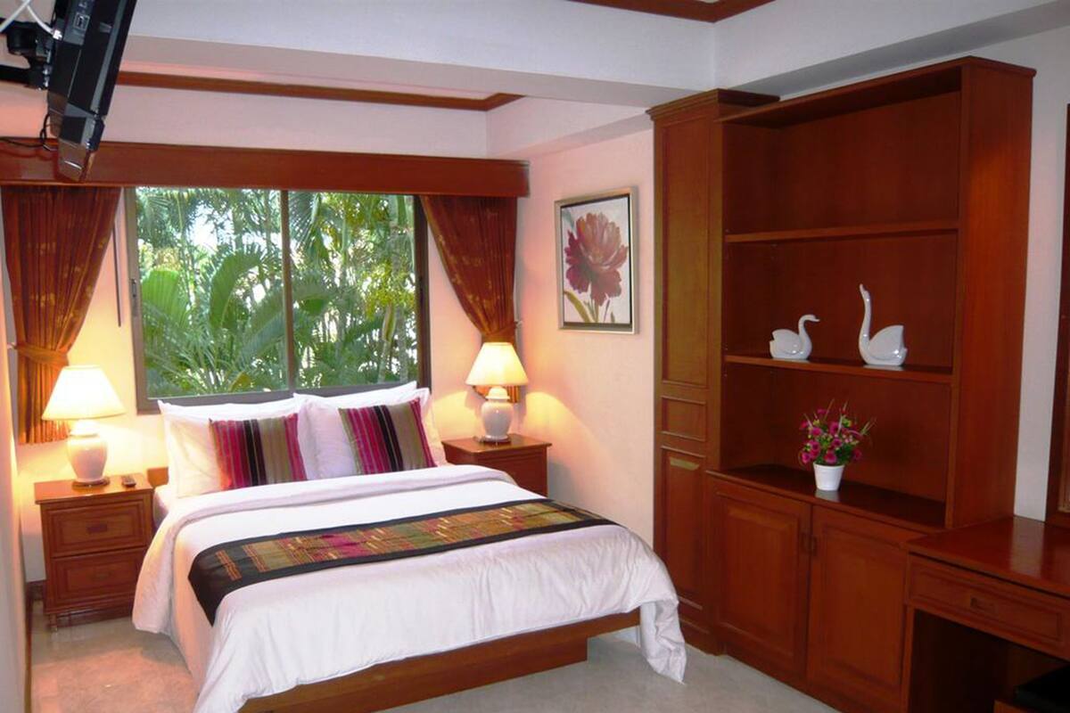 A bedroom with a bed, two bedside tables with lamps, a wooden wardrobe, and a window with curtains.