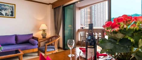 Habitación de hotel con sofá, una mesa de comedor con una botella de vino, una planta en maceta y vistas a un paisaje urbano.