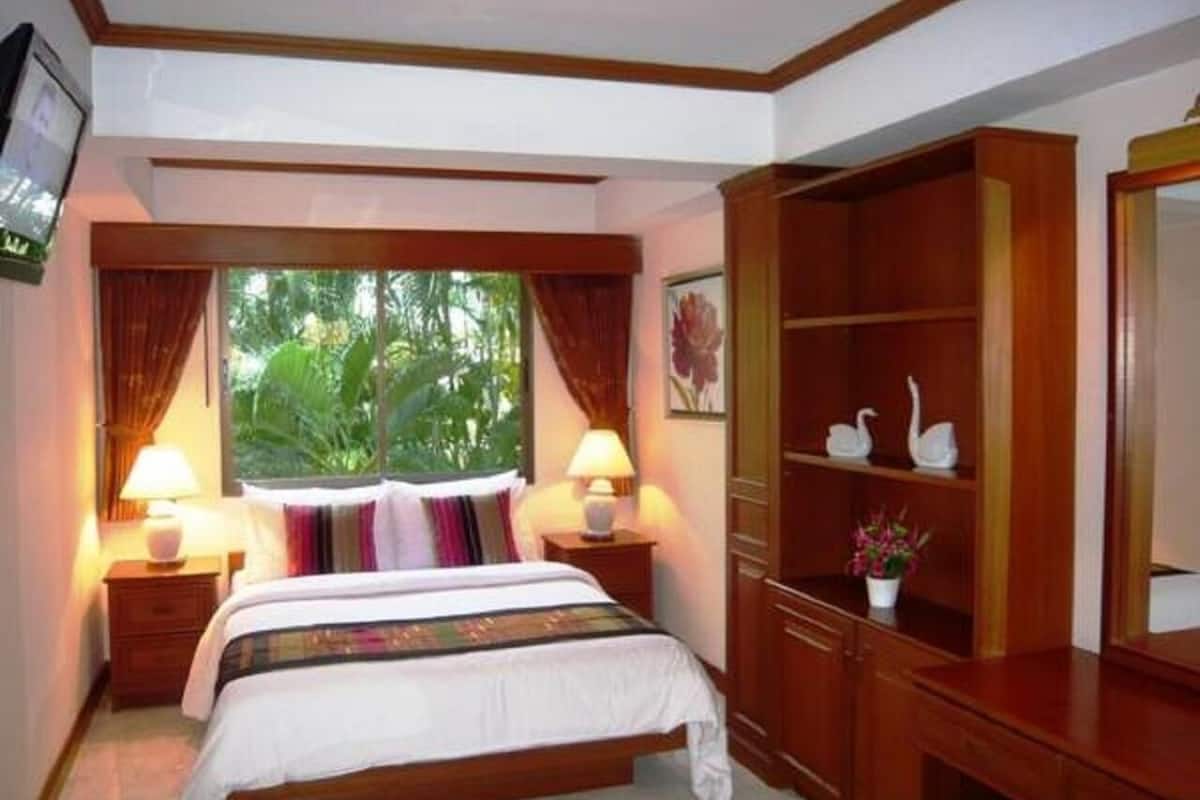 A hotel room with a large bed, two bedside lamps, a wooden wardrobe, and a window with curtains.
