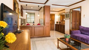 Amplia sala de estar con una mesa baja de madera, un sofá púrpura y una zona de cocina con armarios de madera y un refrigerador.