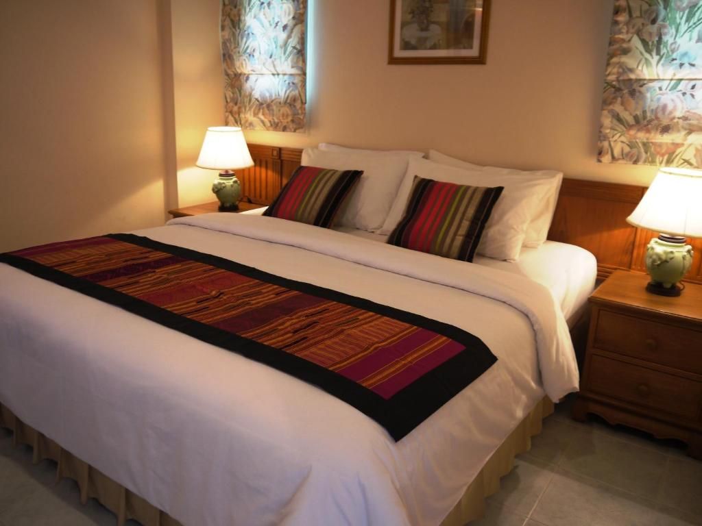 Een netjes opgemaakt bed met een bedsprei met dessin, twee bedlampen en een bloemrijk schilderij aan de muur.
