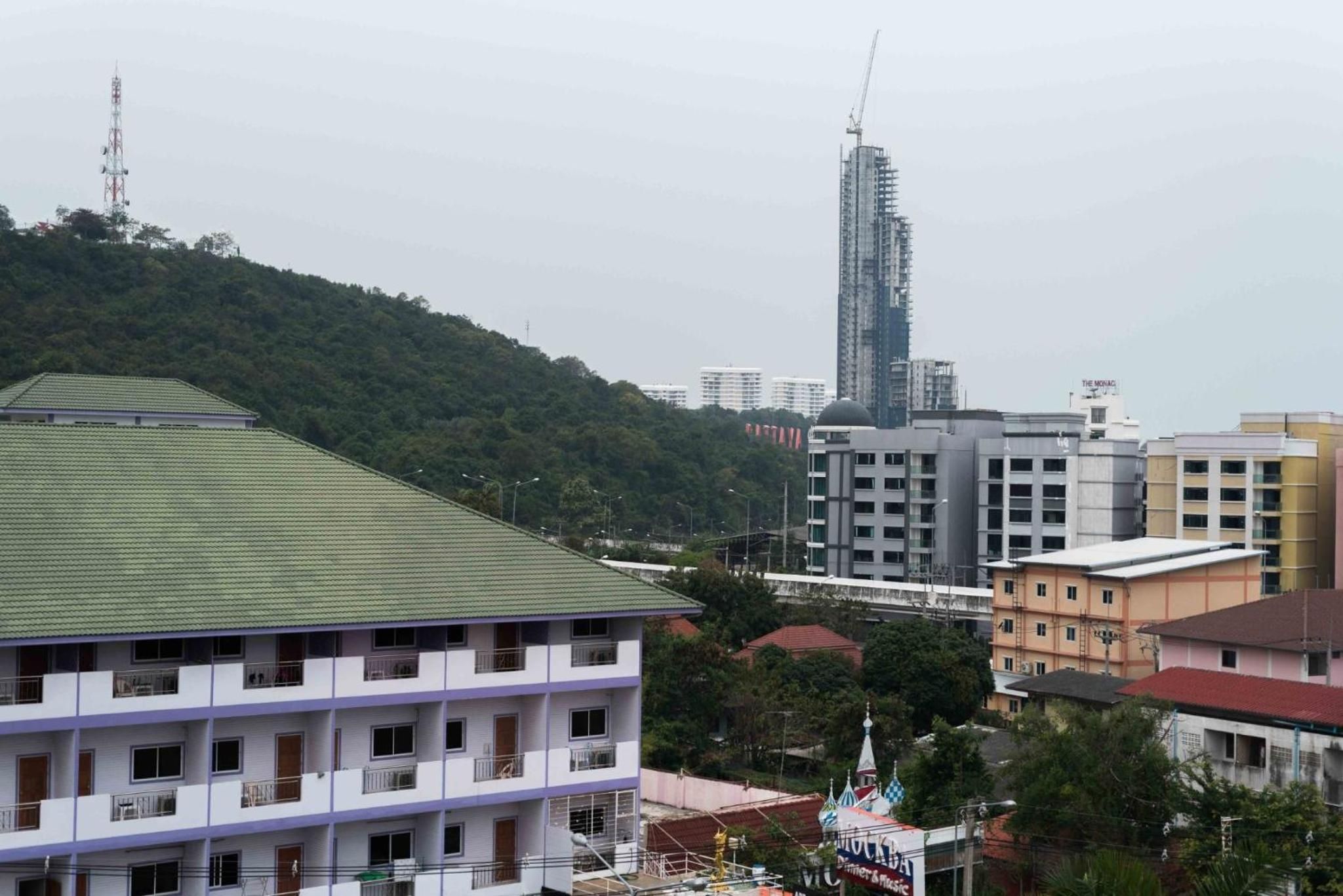 Un edificio de varios pisos con techo verde, rodeado de otros edificios y una colina.