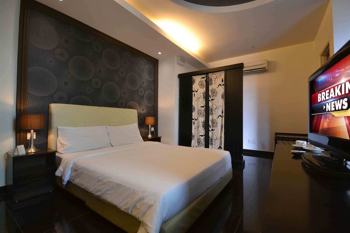 A hotel room with a large bed, two bedside tables with lamps, a TV, and a patterned wall.