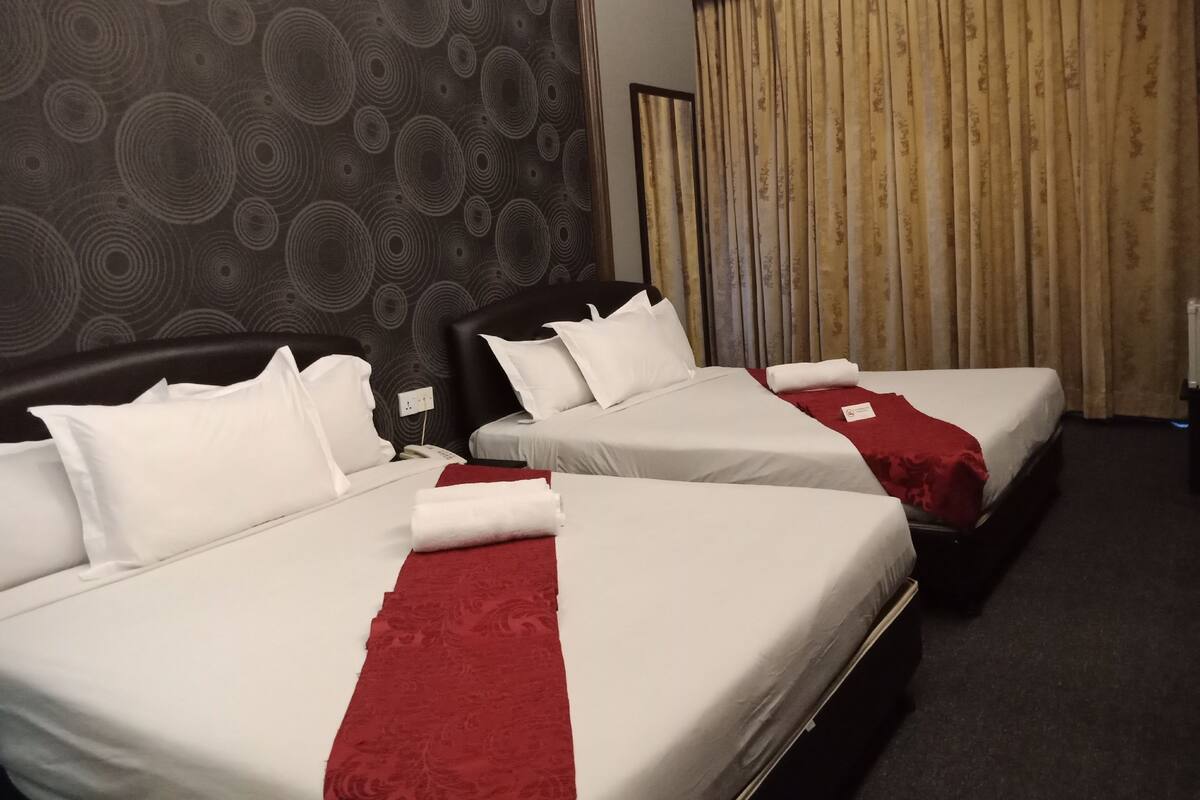 A hotel room with two beds, a dark patterned wall, and a curtain.