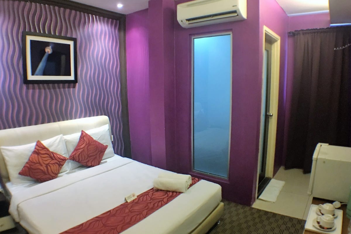 A hotel room with a bed, a wardrobe, an air conditioning unit, and a small table with a teapot.