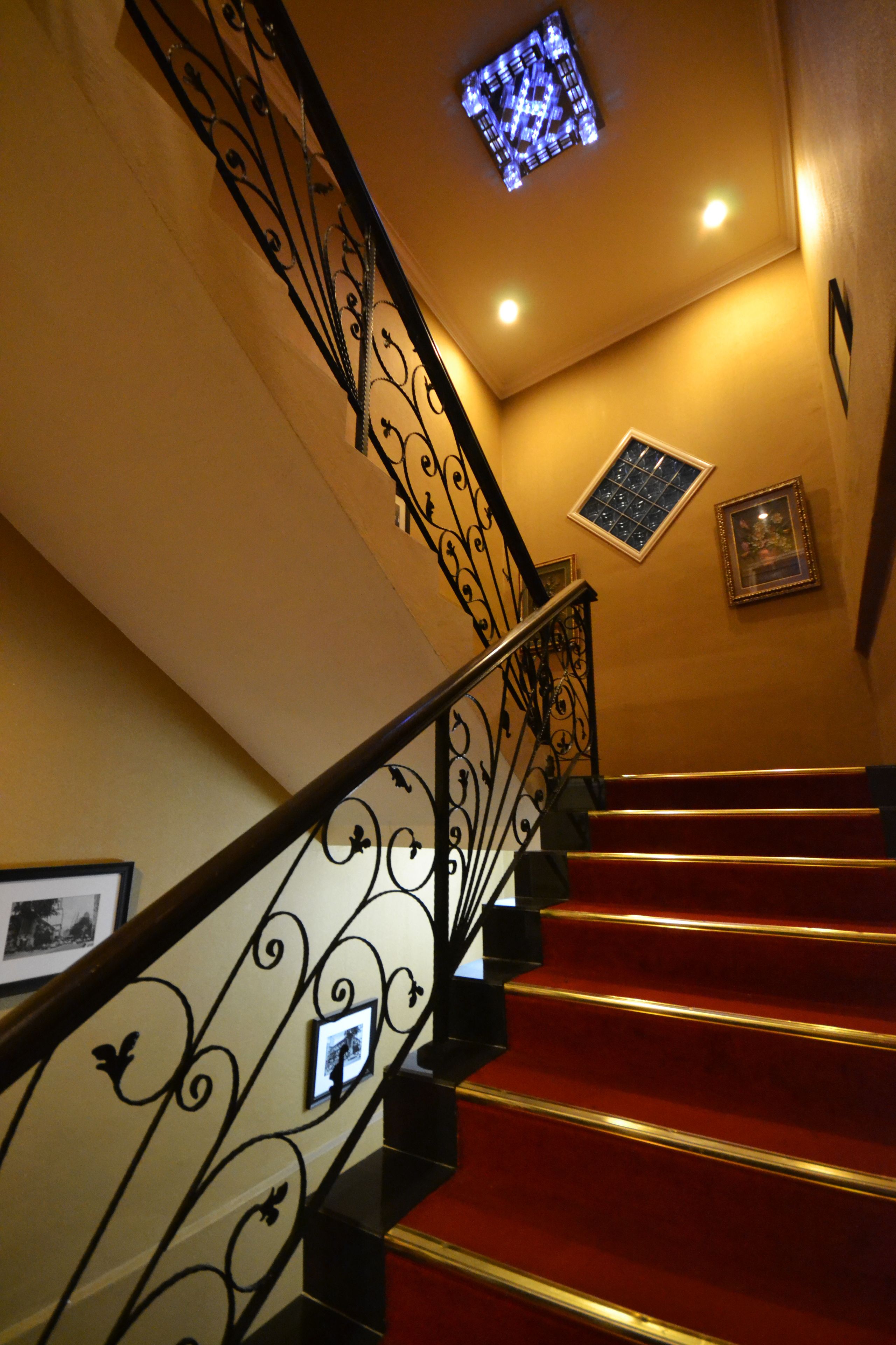 A staircase with ornate black railings and red steps, a small window, and framed pictures on the walls.