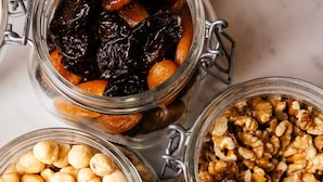 Cuatro frascos de vidrio con cierres metálicos que contienen distintos tipos de nueces y frutas secas.
