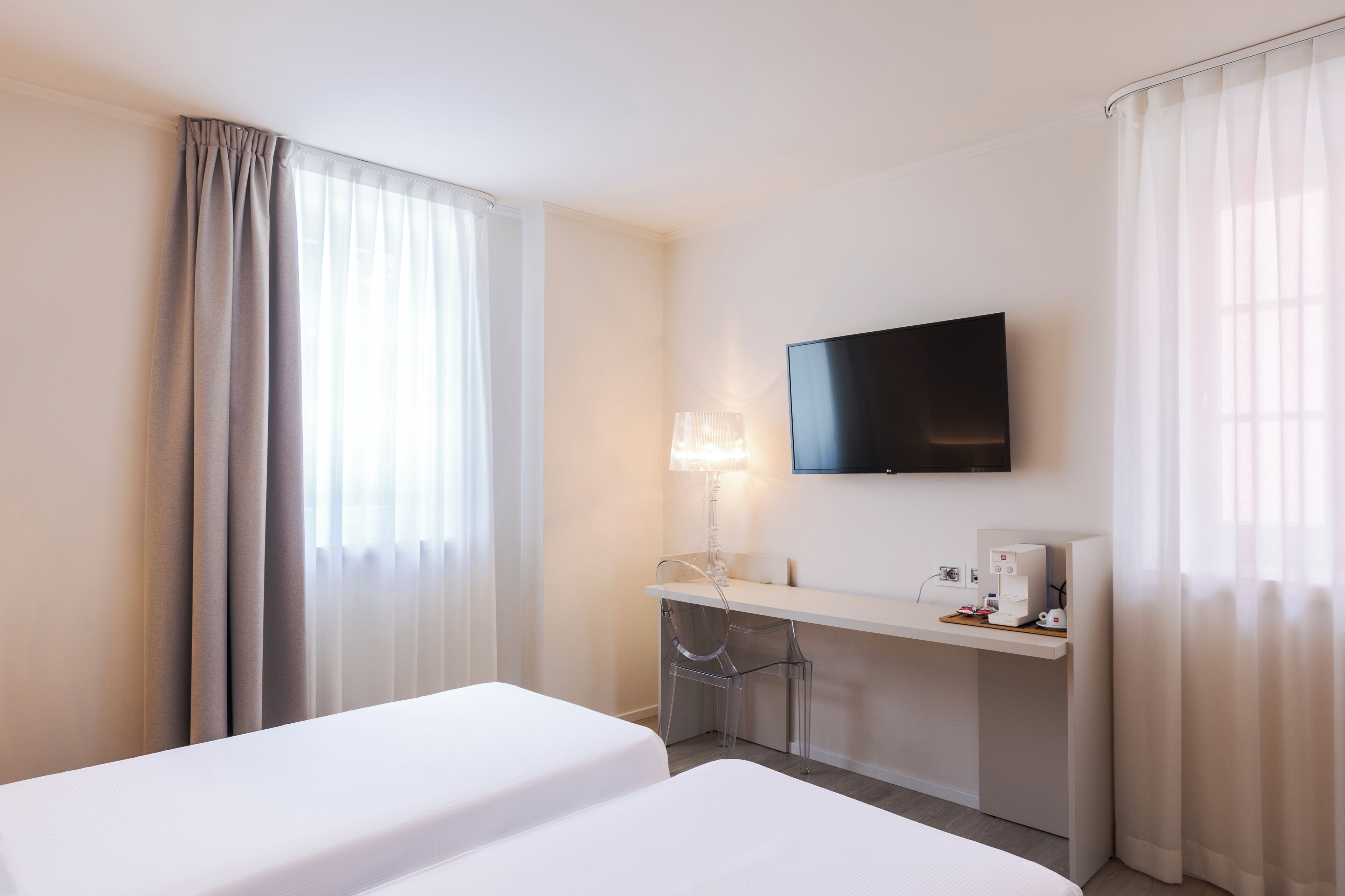 Ein Hotelzimmer mit zwei Betten, einem Fernseher, einem Schreibtisch mit Lampe und einer Kaffeemaschine.