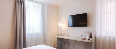 A hotel room with two beds, a TV, a desk with a lamp, and a coffee machine.