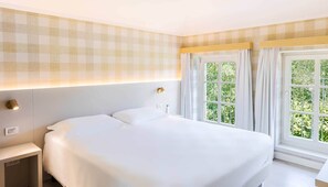Une chambre d’hôtel avec un grand lit, deux lampes de chevet, une fenêtre avec des rideaux et un mur orné d’un motif à carreaux.