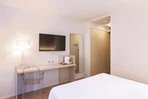 Habitación de hotel con cama, escritorio con lámpara, cafetera, televisor y armario.