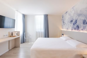 A modern hotel room with a large bed, a flat-screen TV mounted on the wall, a desk with a coffee machine, and a large abstract painting on the wall.