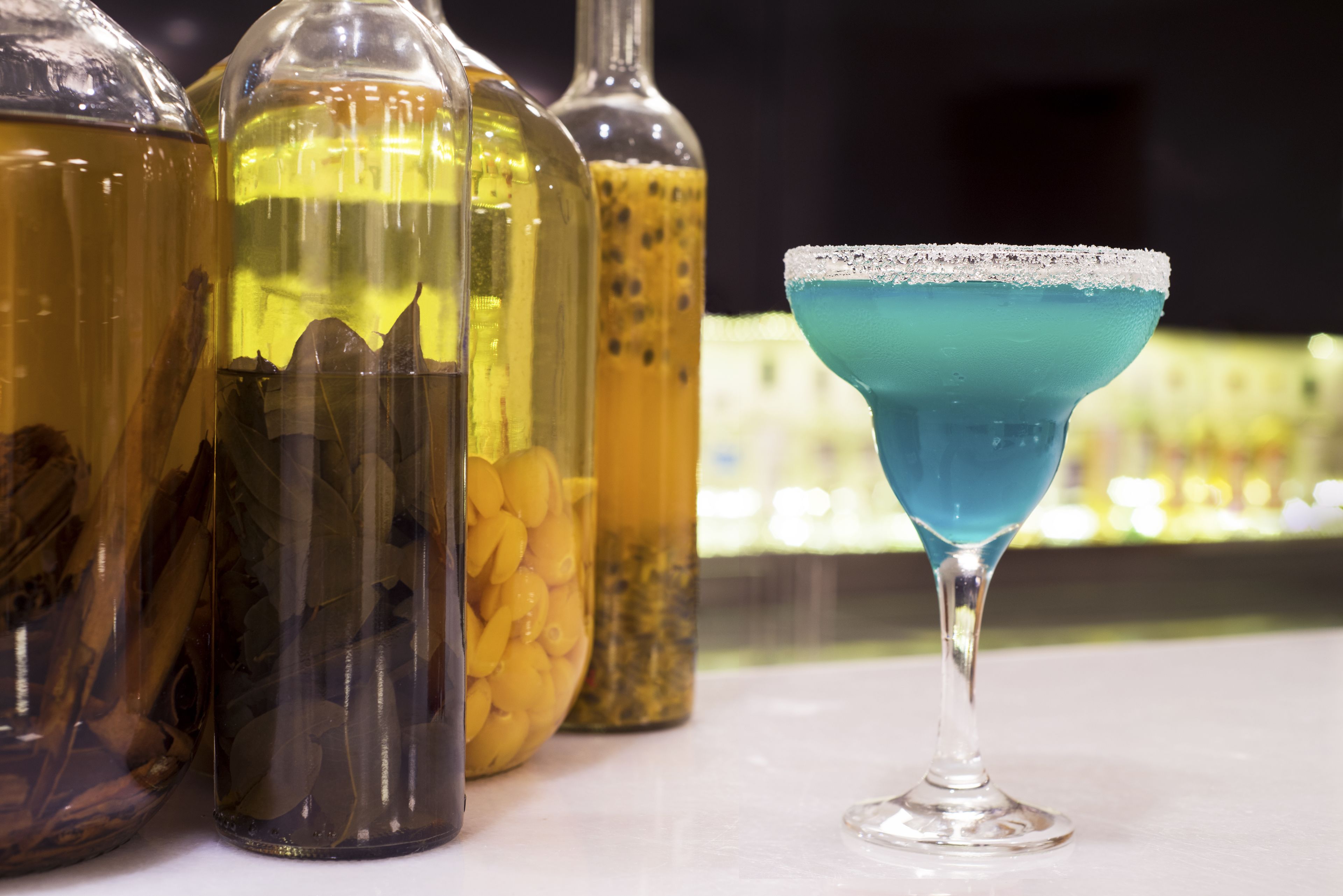Un vaso para cóctel con un líquido azul y un borde de sal, rodeado de botellas con diferentes contenidos.