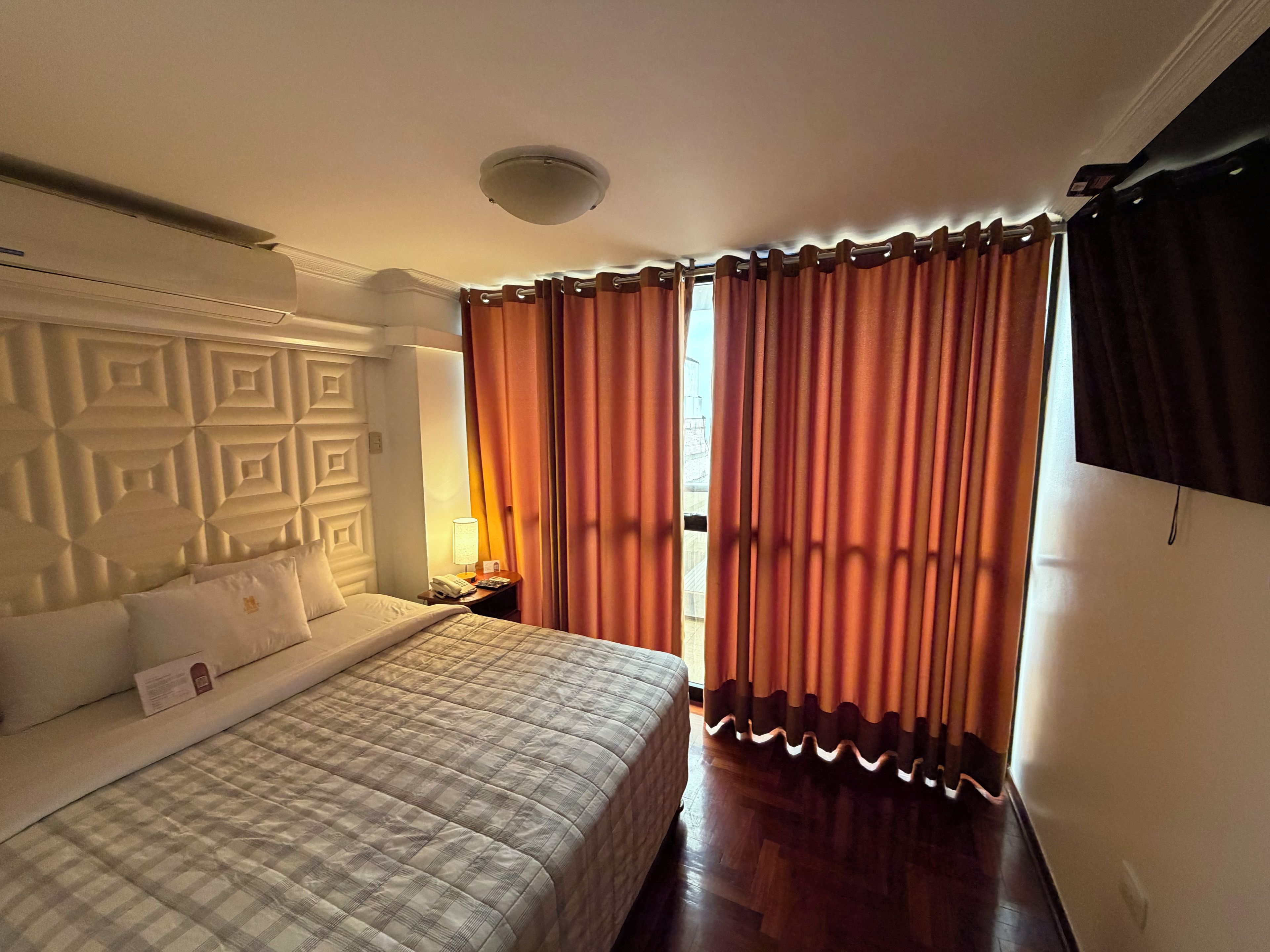 A hotel room with a bed, a nightstand, a lamp, and a window with curtains.