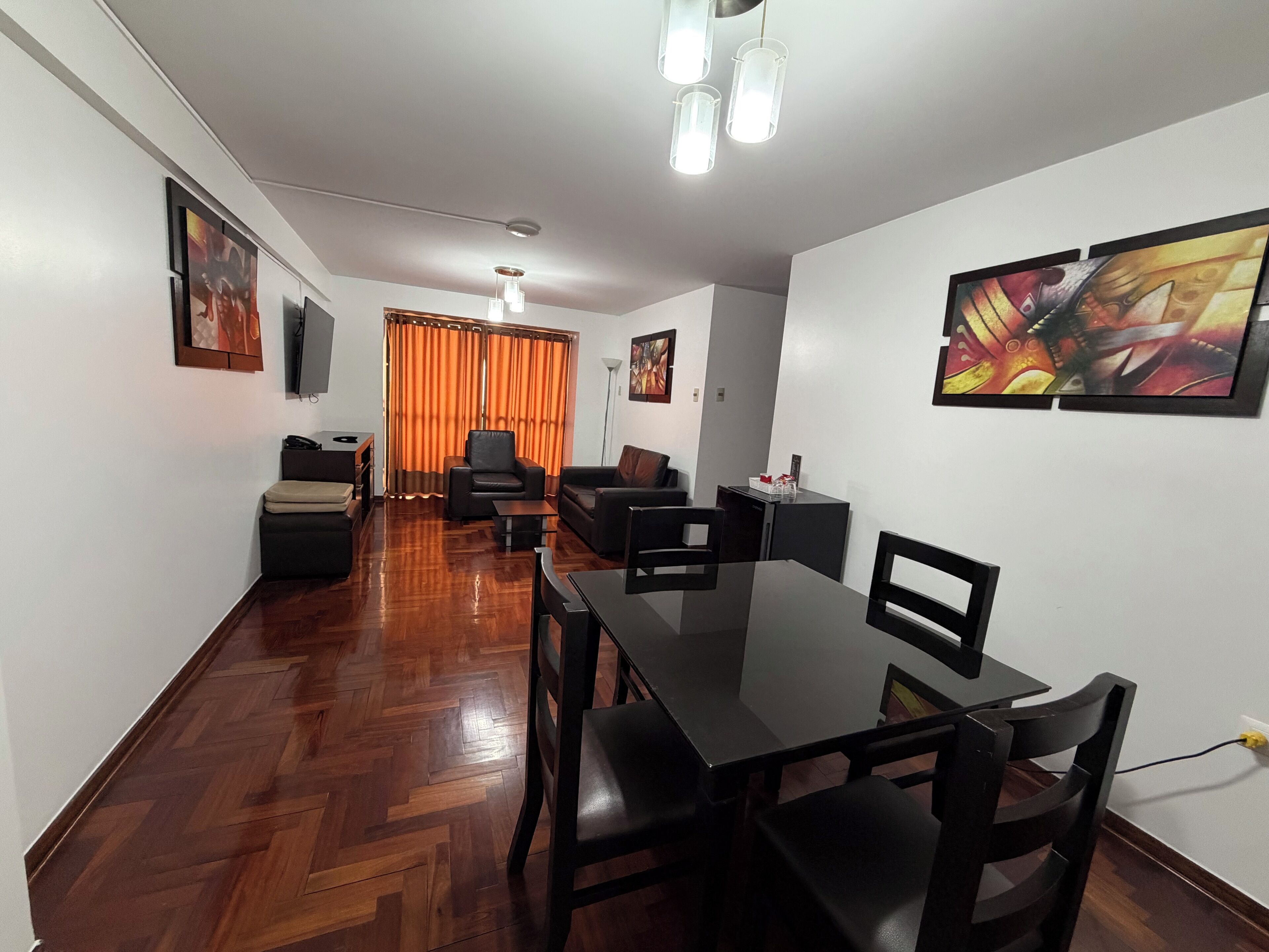 A modern living room with a herringbone floor, a dining table with chairs, a sofa, and a television.