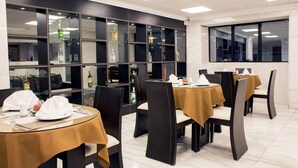 Un ristorante con diversi tavoli, sedie scure e una parete divisoria in vetro con bottiglie.
