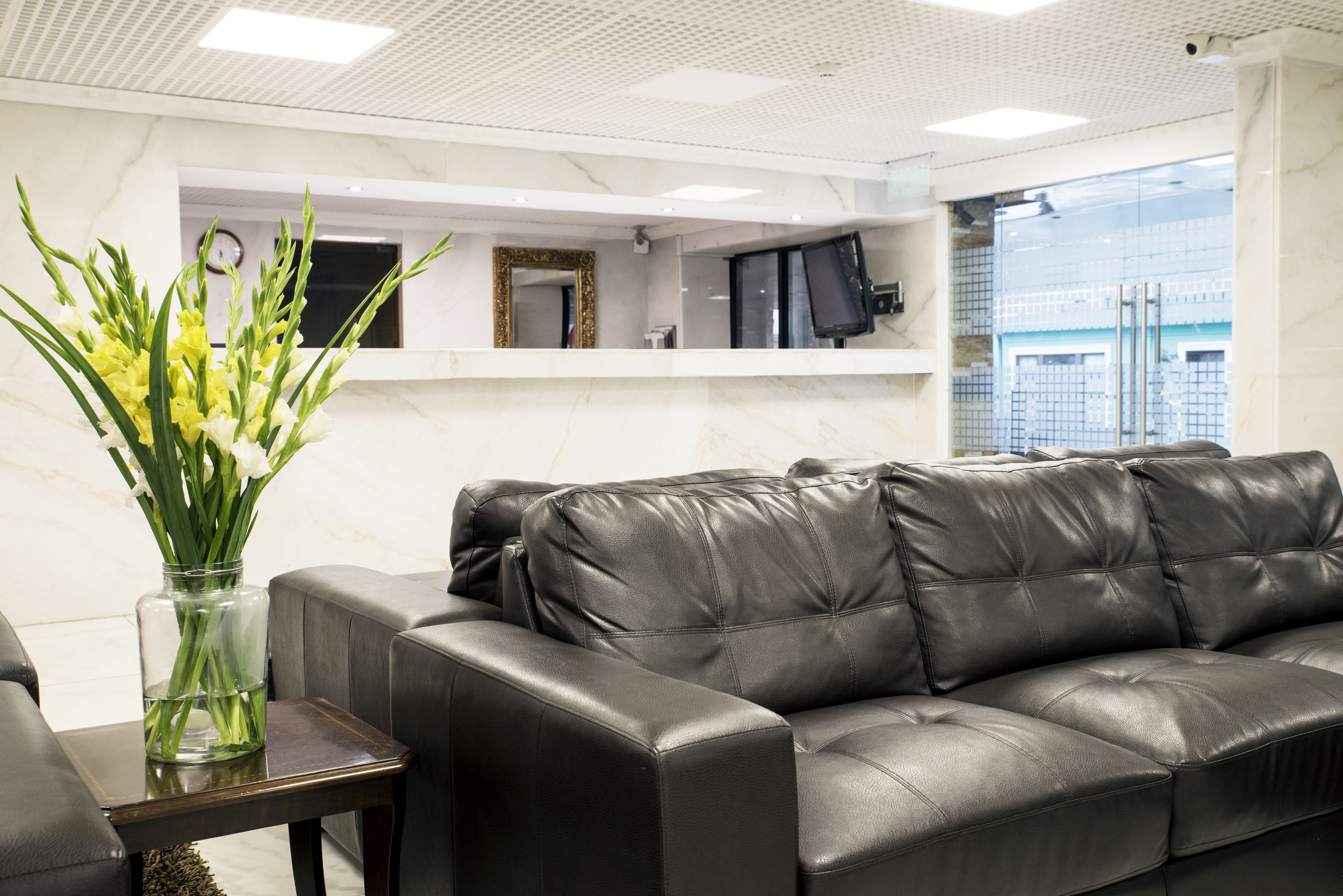 A modern living room with a black leather sofa, a glass vase with flowers, and a marble wall.