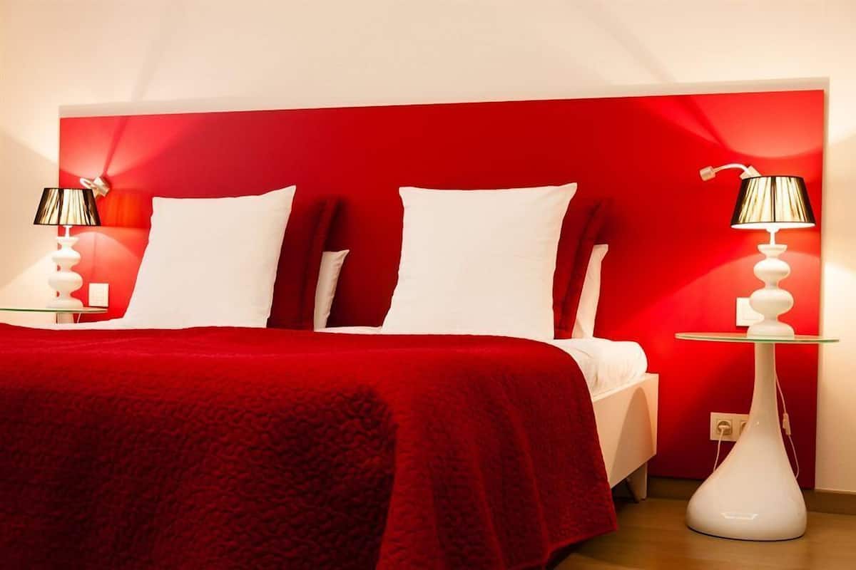 A hotel room with a red headboard, white bedding, and two bedside tables with lamps.
