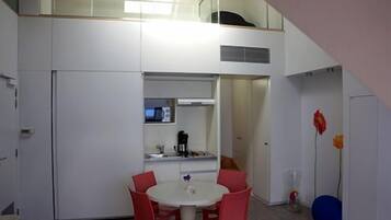 A compact room with a kitchenette, a dining area with red chairs, and a small window.
