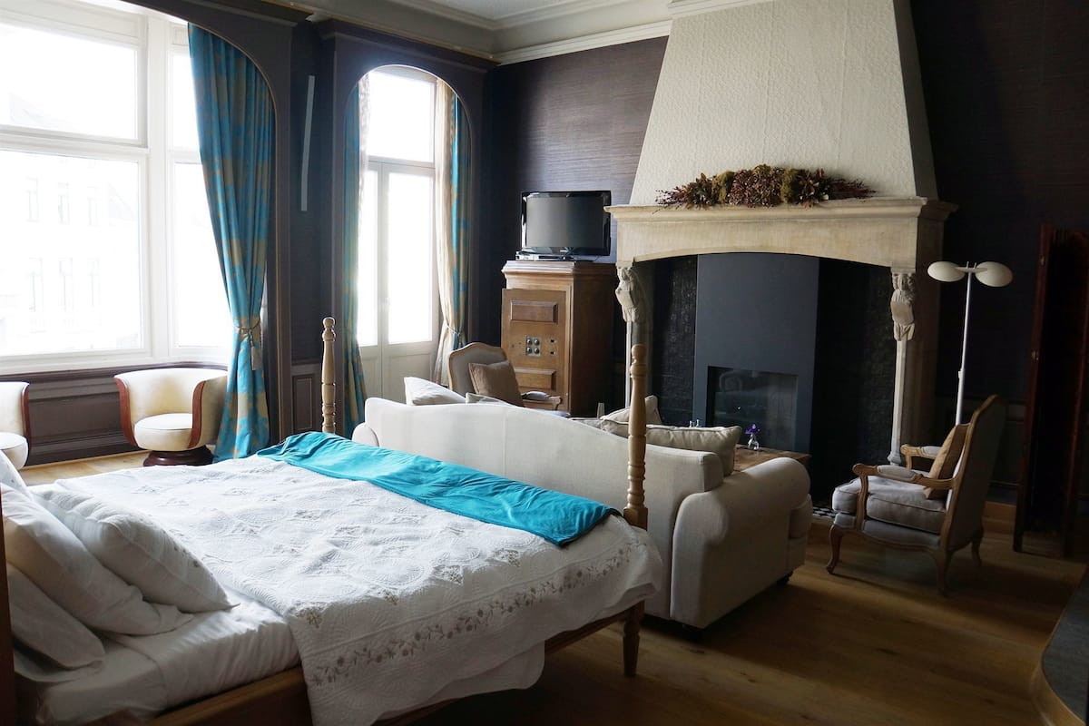 A hotel room with a large bed, a fireplace, a television, and a seating area with chairs.
