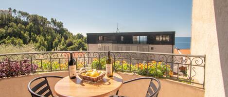 A balcony with a round table, two chairs, a bottle of wine, and a basket of lemons.