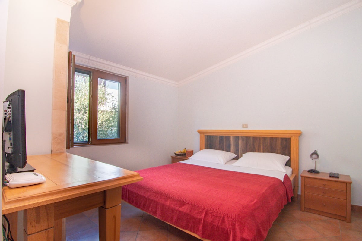 Ein Schlafzimmer mit einem Bett, einem Schreibtisch, einem Computer, einem Fenster und einem Nachttisch.