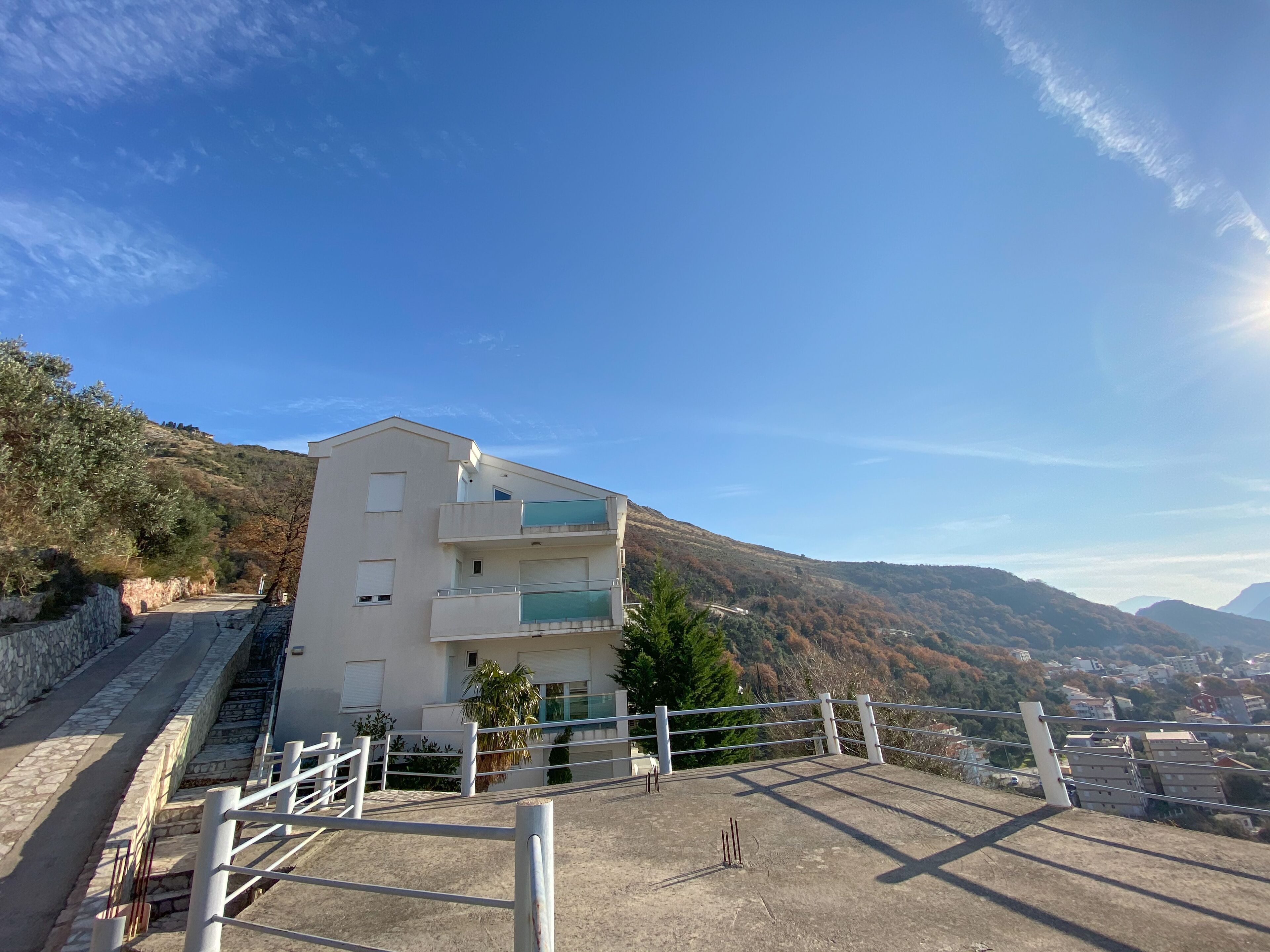 A modern building with multiple balconies and a view of a town and mountains in the background.