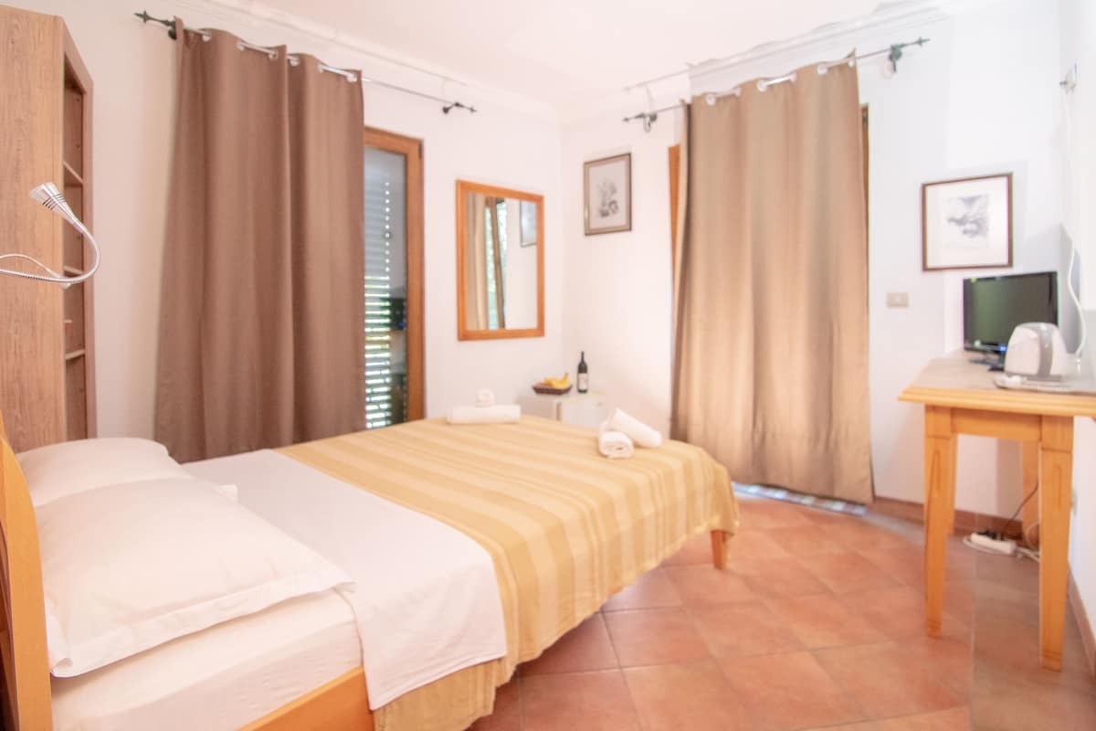 Ein Hotelzimmer mit Bett, Schreibtisch, Stuhl, Fernseher und einem Fenster mit Vorhängen.