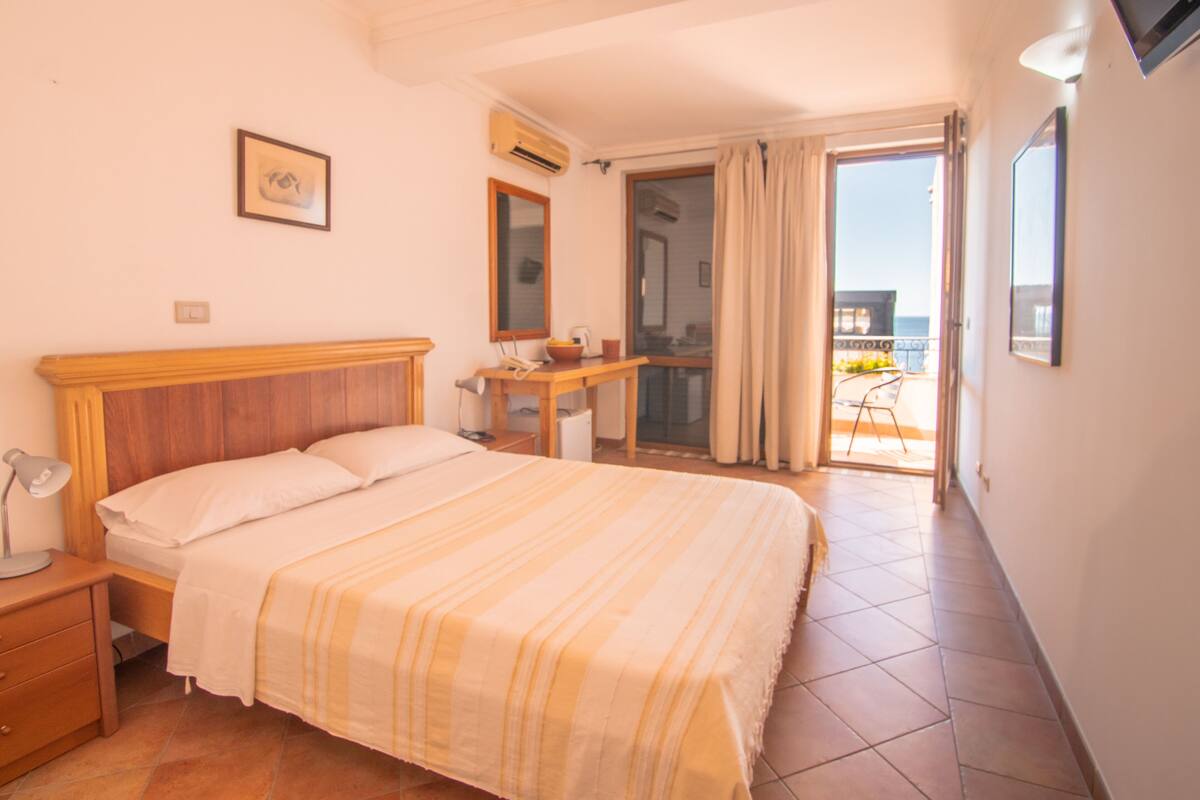 Ein Hotelzimmer mit Bett, Nachttisch, Schreibtisch und Blick auf den Balkon.