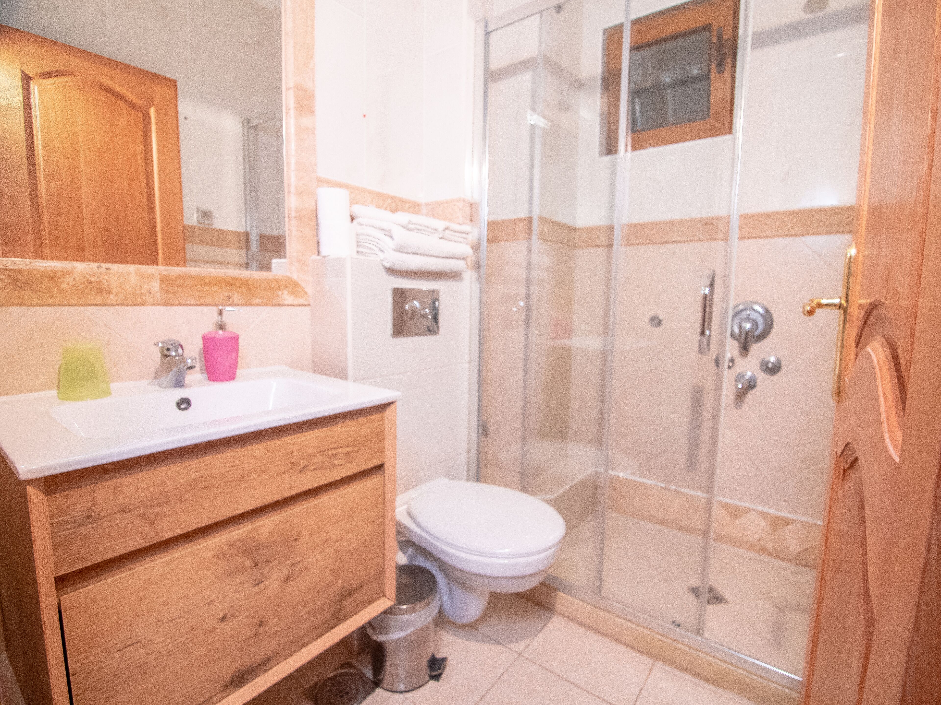 Un baño con tocador de madera, lavamanos, inodoro y zona de ducha con mampara de vidrio.