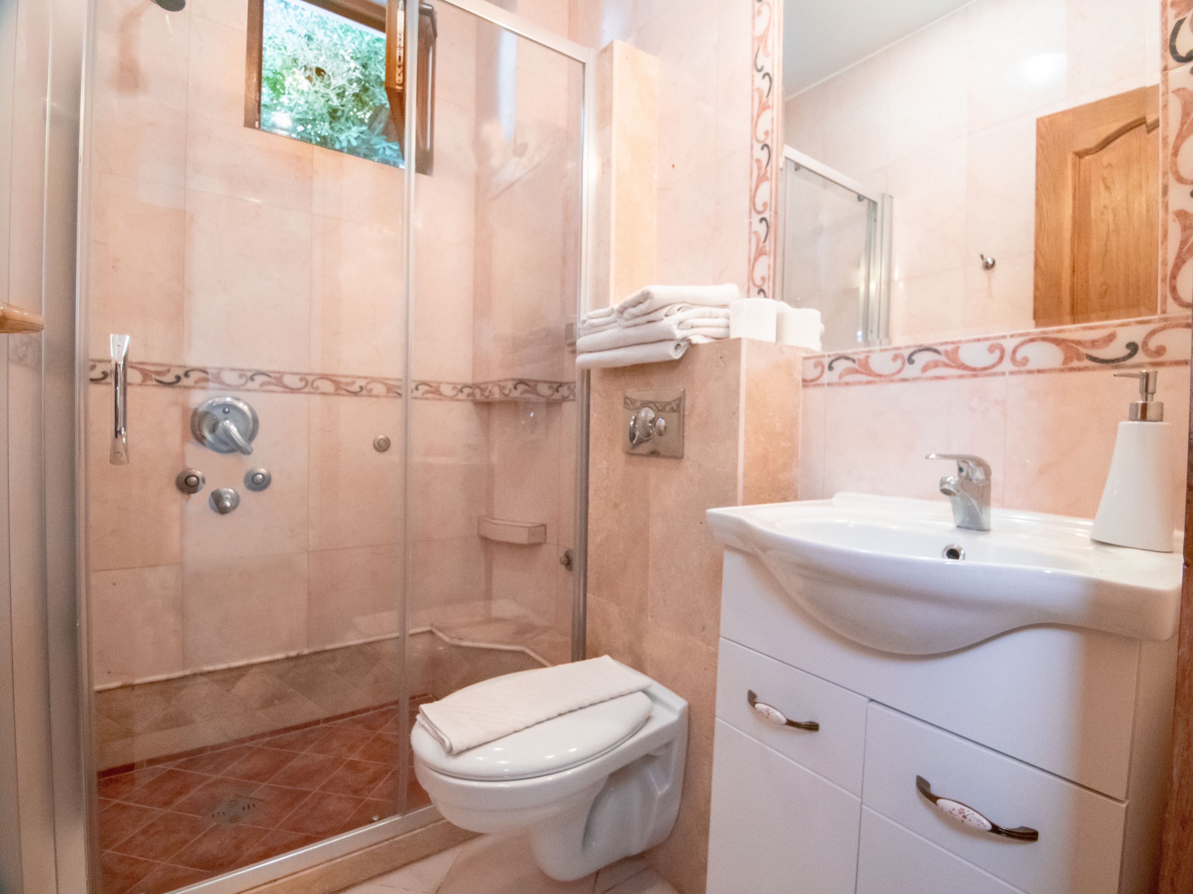 A bathroom with a glass-enclosed shower, a toilet, a sink, and a mirror.