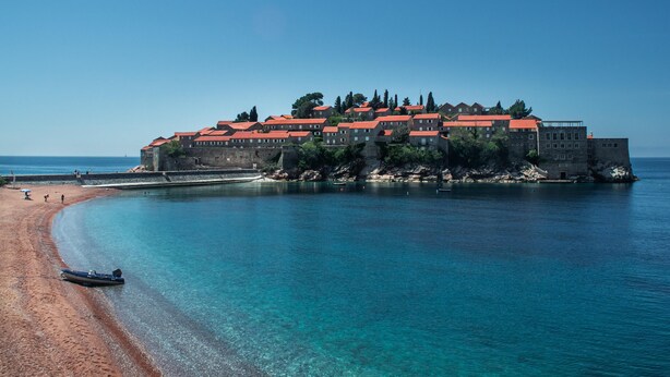 Edifici costaner amb teulada vermella, ubicat sobre una platja sorrenca amb aigües blaves i transparents.