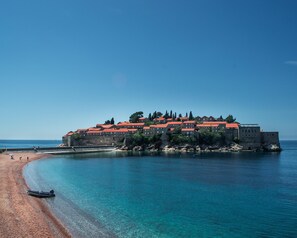 A coastal building with a red roof, situated on a sandy beach with clear blue waters. - Levantin Inn (Sveti Stefan)