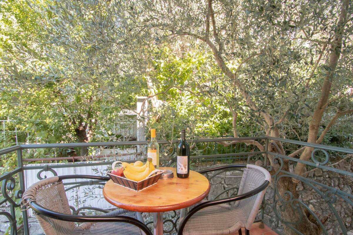 Ein Balkon mit Korbstühlen und einem kleinen runden Tisch, mit einer Weinflasche, einem Obstkorb und einer Schale.