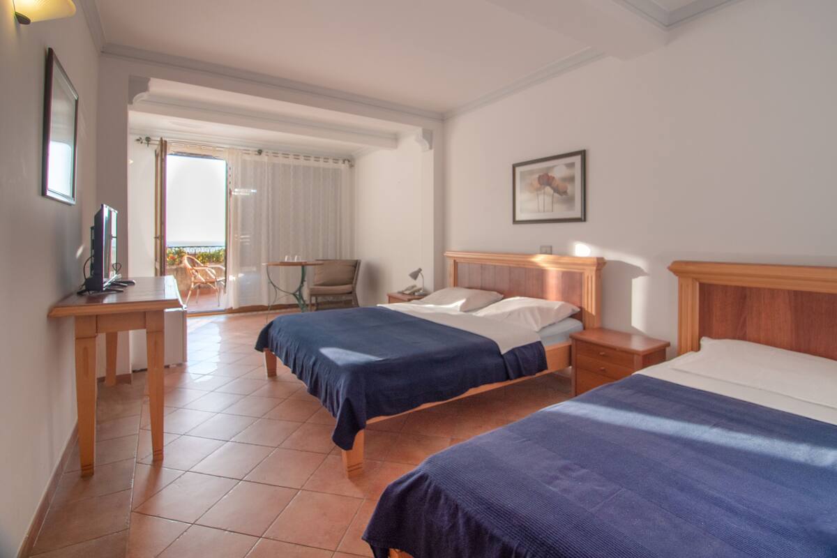 Ein Hotelzimmer mit zwei Betten, einem Schreibtisch, einem Stuhl und einem Balkon mit Blick.