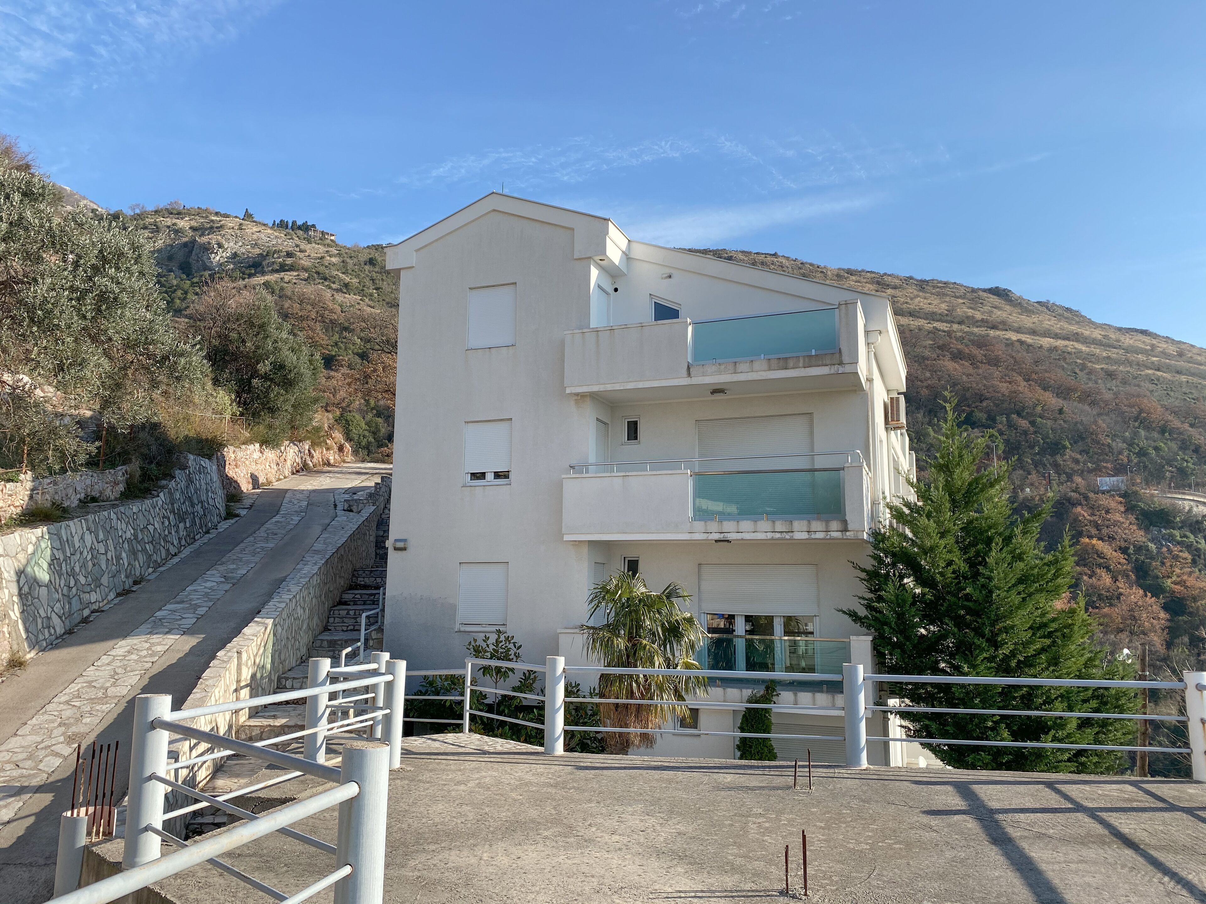 Un immeuble moderne à plusieurs étages, doté de balcons, d’un mur de soutènement en pierre et offrant une vue sur un paysage vallonné.