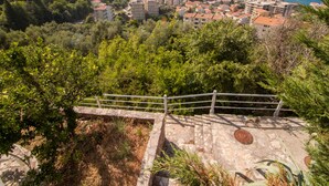 Un poble costaner amb edificis residencials i vegetació, una escala de pedra, i vista al mar.