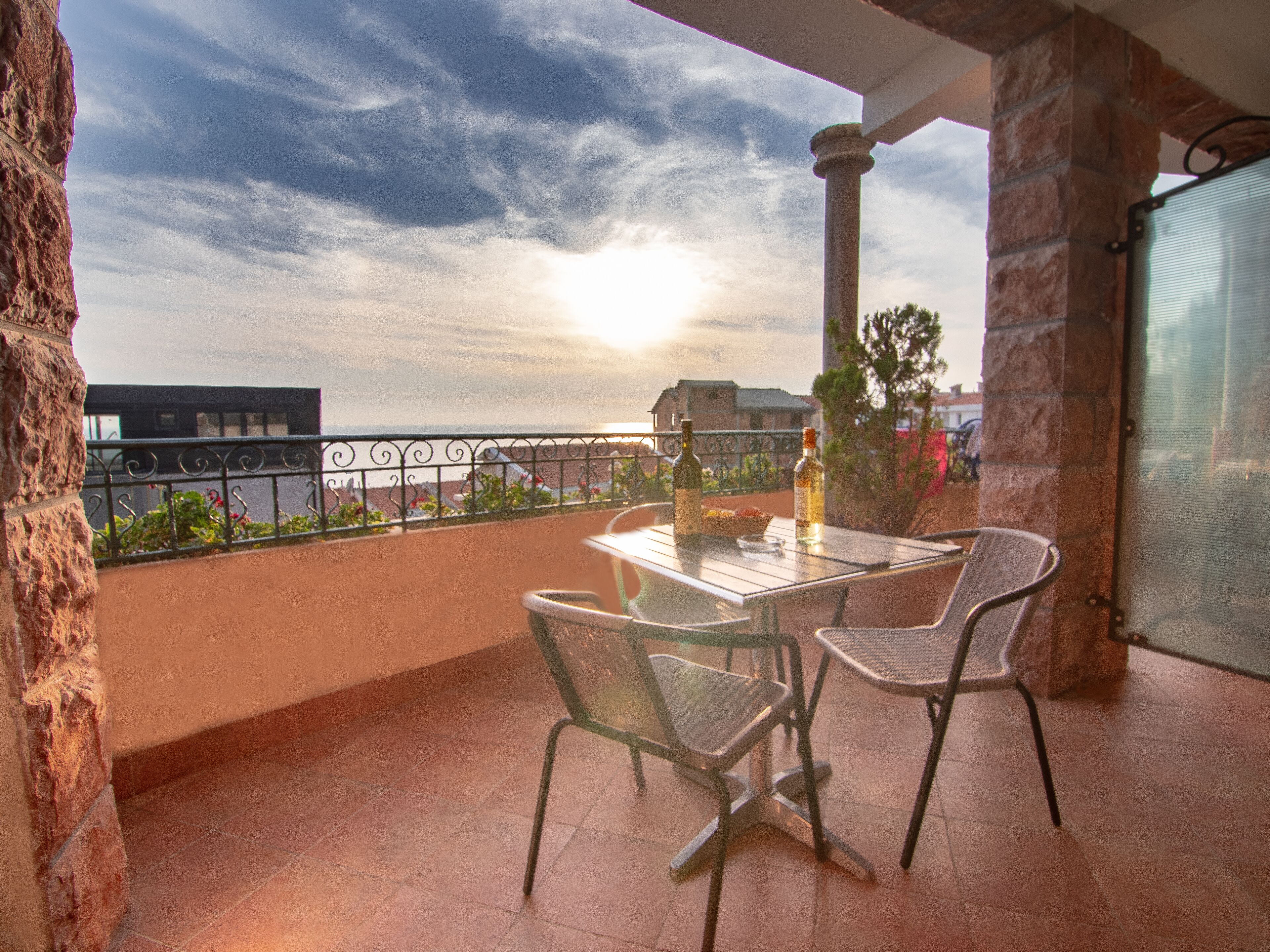 A balcony with a table, two chairs, and two bottles of wine.