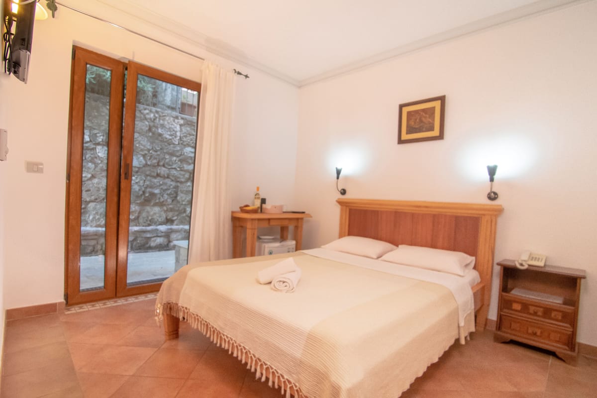 Ein Schlafzimmer mit Bett, Nachttisch, Lampe, einem Bild an der Wand und einer Glastür zum Außenbereich.