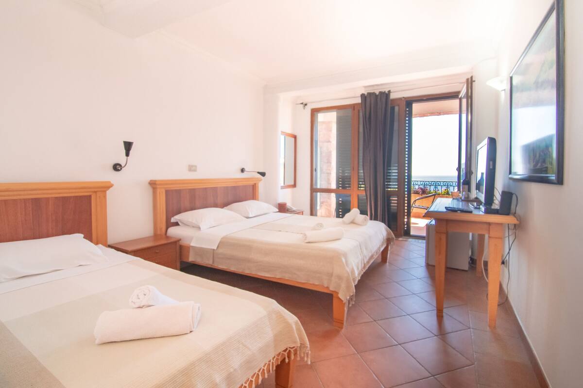 Ein Hotelzimmer mit zwei Betten, einem Schreibtisch, einem Computer und einem Balkon mit Blick.