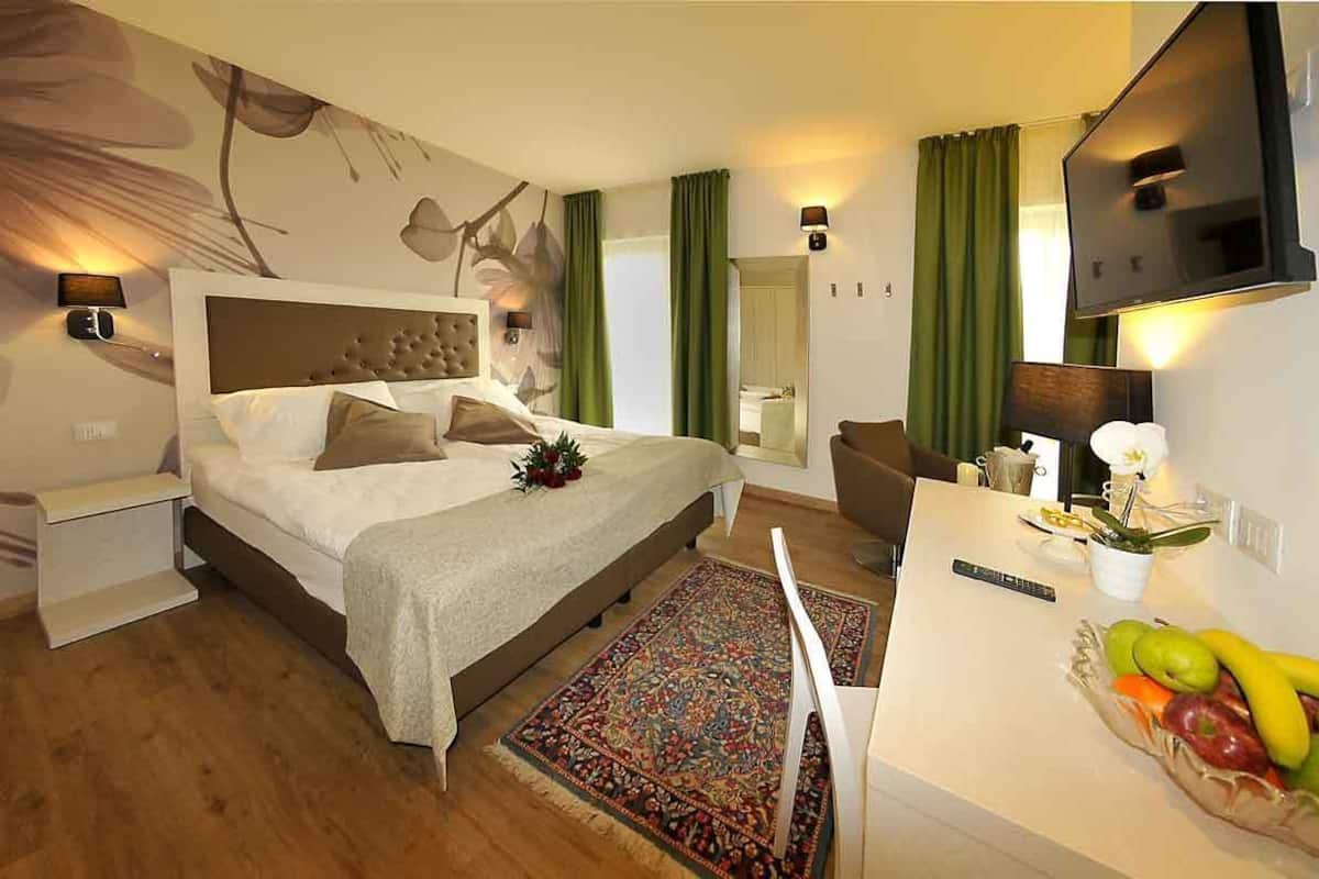 A hotel room with a large bed, a desk with a fruit bowl, a television, and a wall-mounted TV.