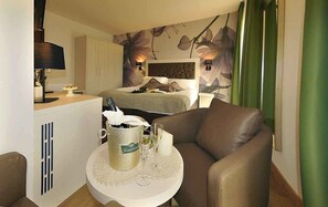 A hotel room with a bed, a small table with a bottle and glasses, a chair, and a wall with floral wallpaper. - Hotel Florida (Levico Terme)
